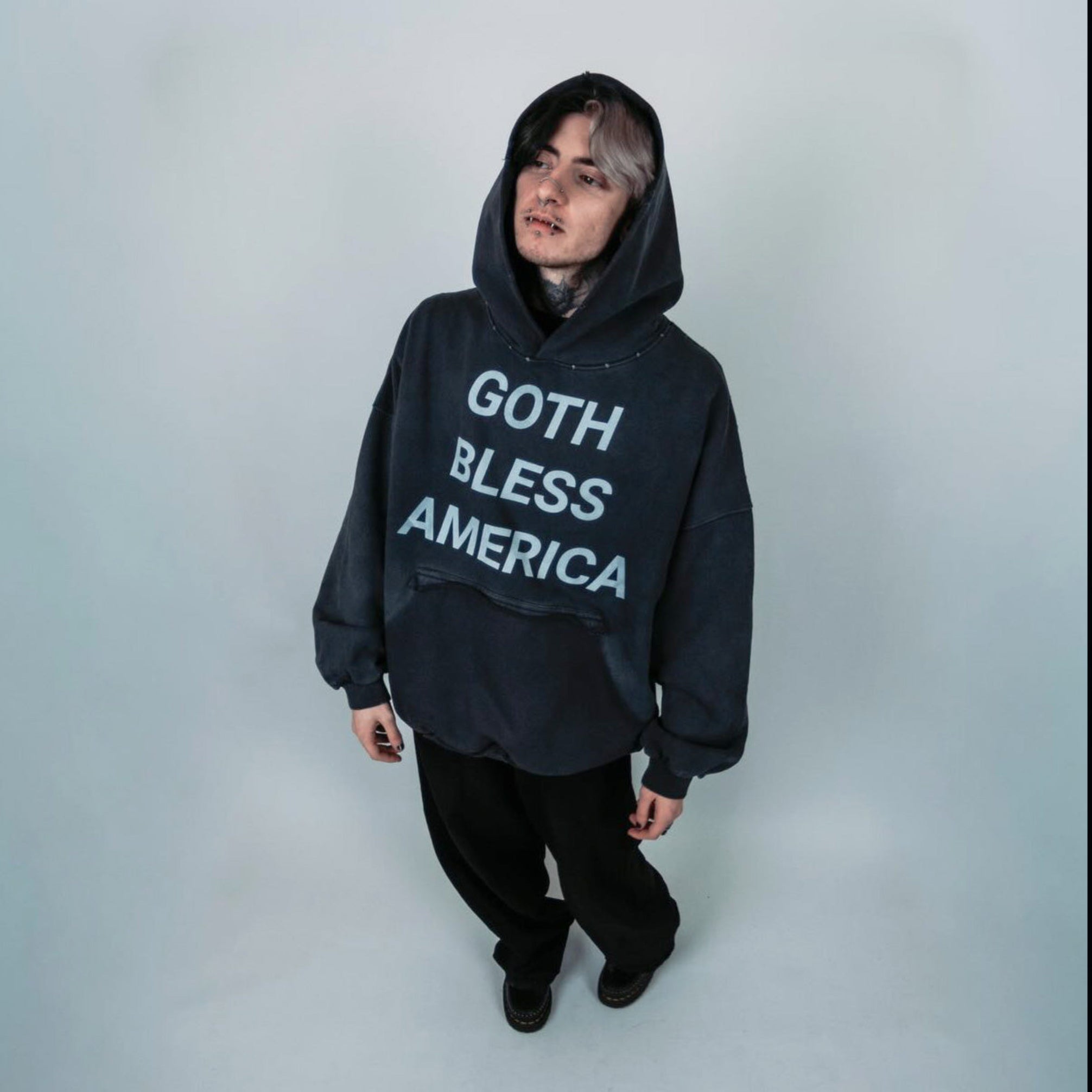Person wearing a black hoodie with 'Goth Bless America' text on a plain background